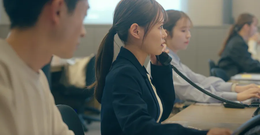 写真：机で電話をとっている女性社員。他にも同じように電話を受ける社員が複数人座っている。